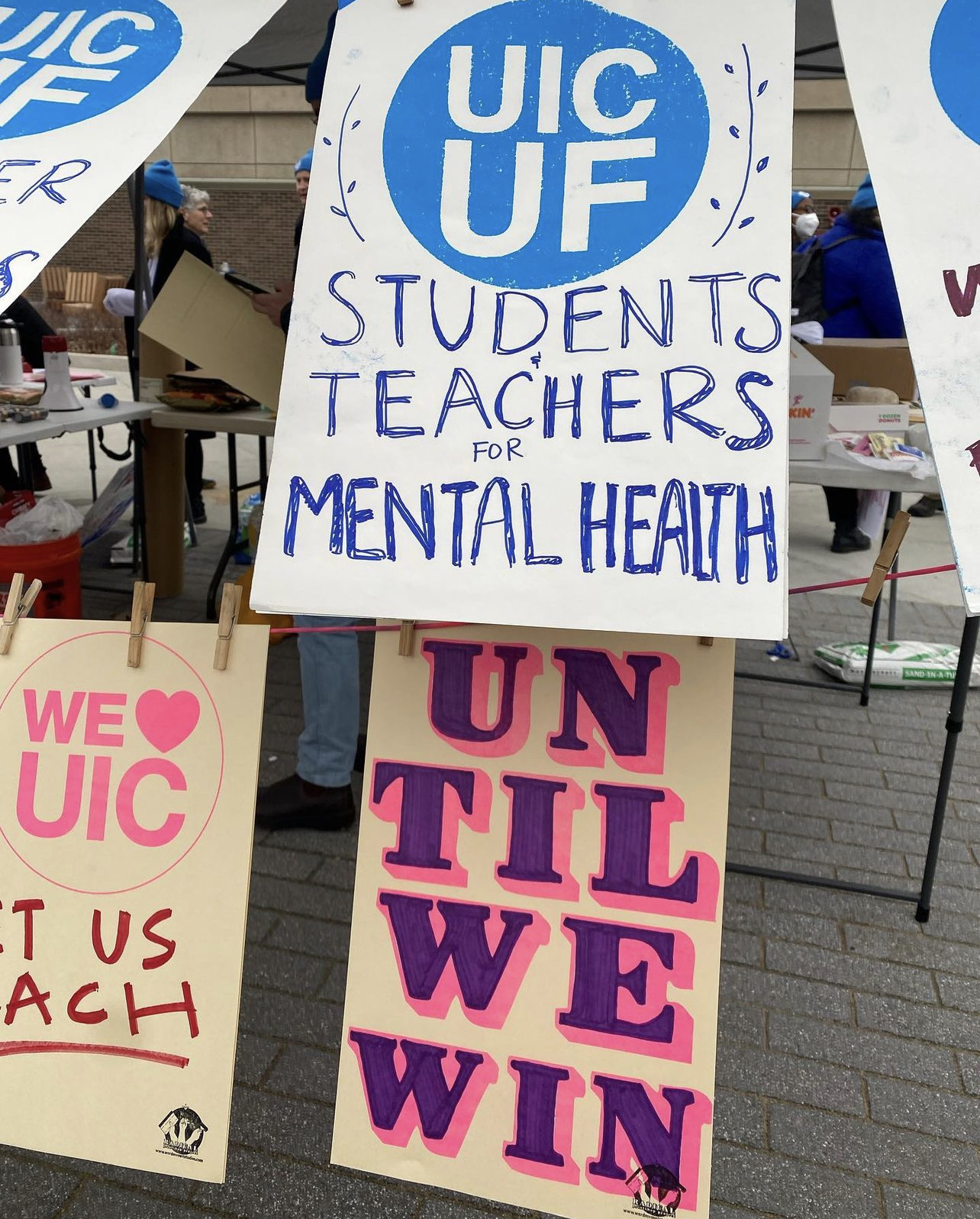Three posters hanging on a dry line that read UIC UF Students and Teachers for Mental Health, We Heart UIC Let Us Teach, and Until We Win.