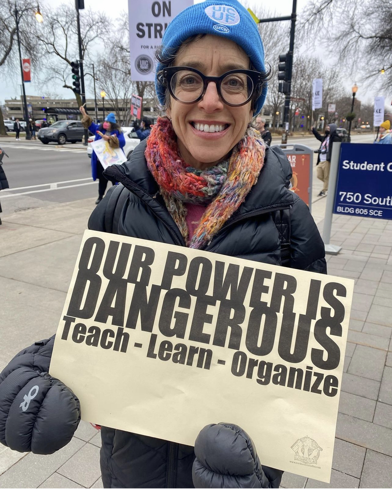 A person with glasses holding an 11 x 17 poster that reads Our Power Is Dangerous, Teach, Learn, Organize.