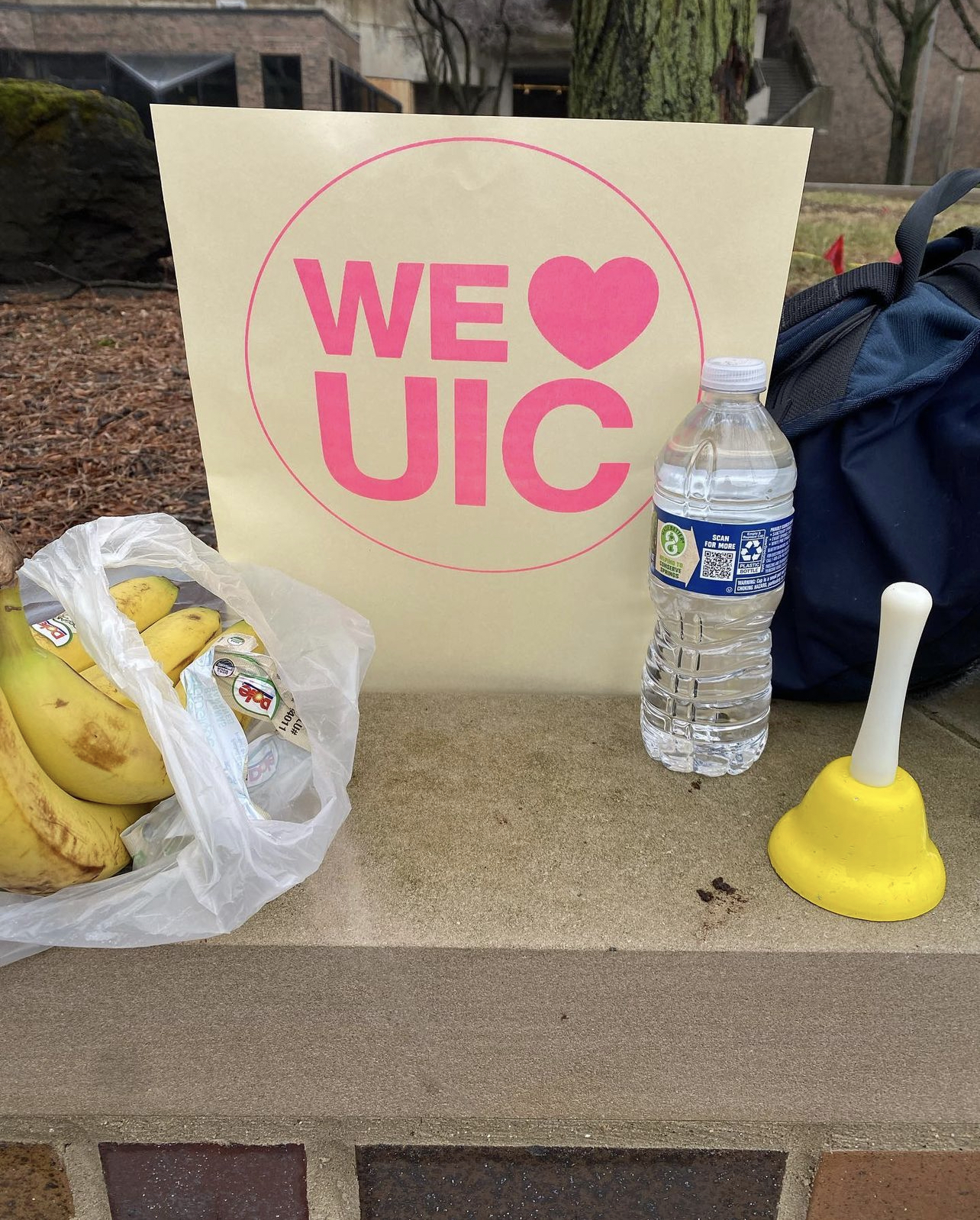11 x 17 poster with text that reads We Heart UIC inside a circle. There are bananas a water bottle, and a plastic toy bell resting on the table around the poster.